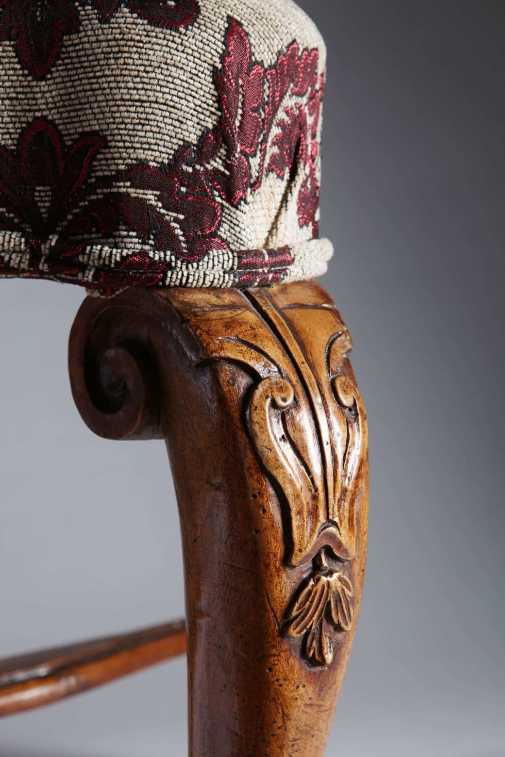 Close-up of ornate carved walnut leg and floral upholstery on an 18th century Italian stool by Collection CK20.
