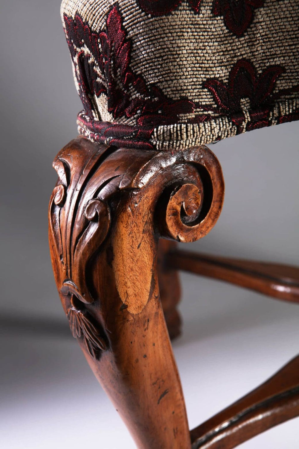Close-up of an 18th century Italian walnut stool leg with intricate carving and floral upholstery by Collection CK20