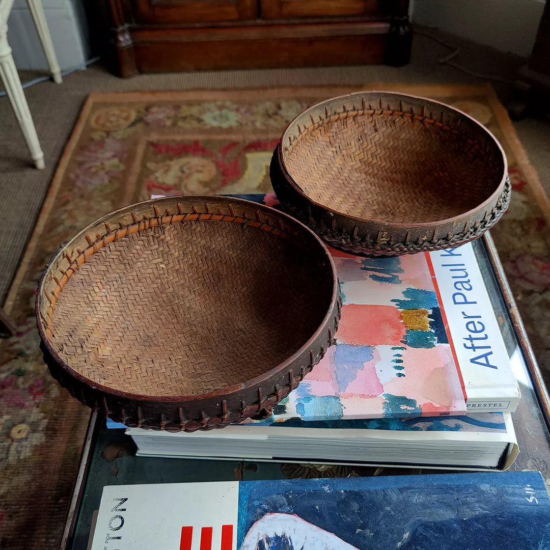 Two round woven bamboo rattan bowls by Nicholas Wells Antiques resting on art books in a cozy room setting