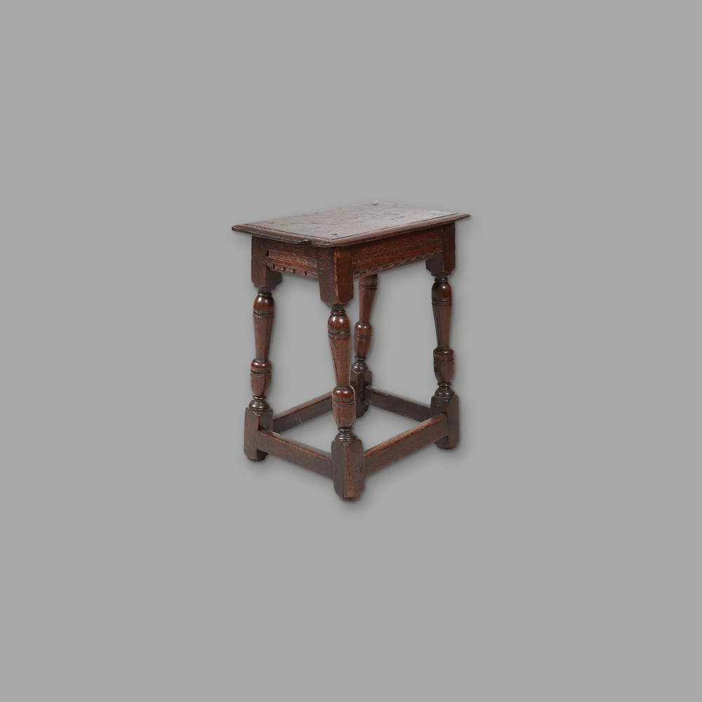 Early 17th Century Oak Joint Stool, on a plain mid-grey background.