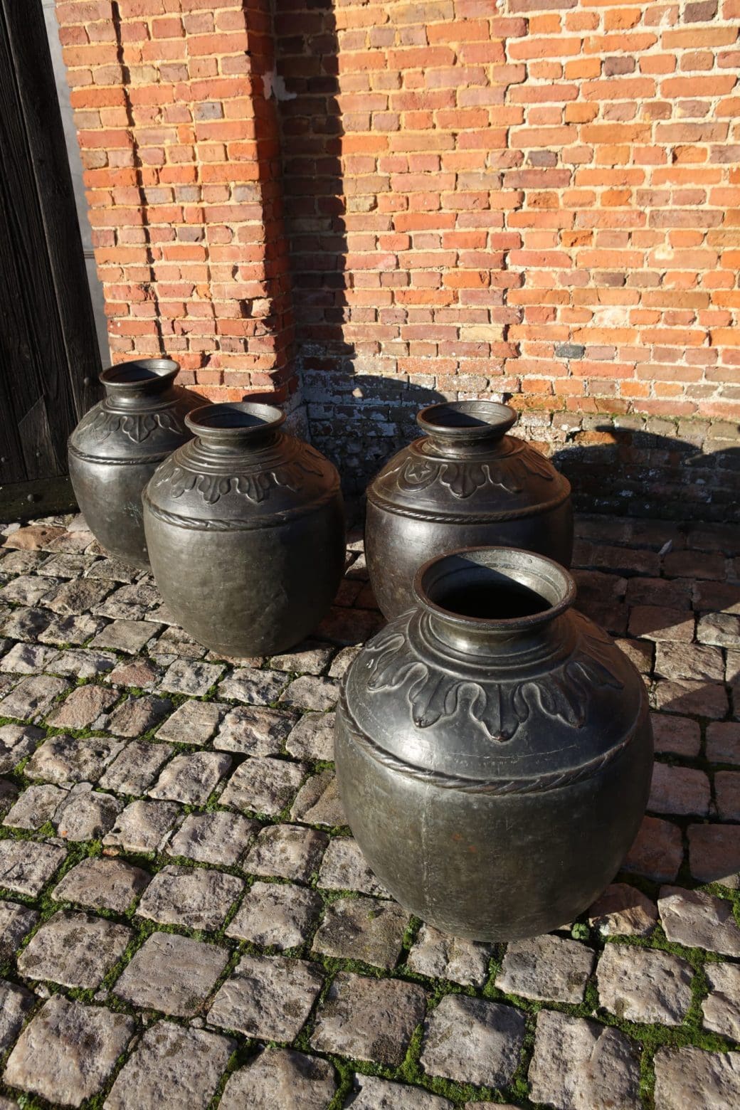 A set of four large vintage Sindh bronze pots on cobblestone with brick wall background by Collection EE10