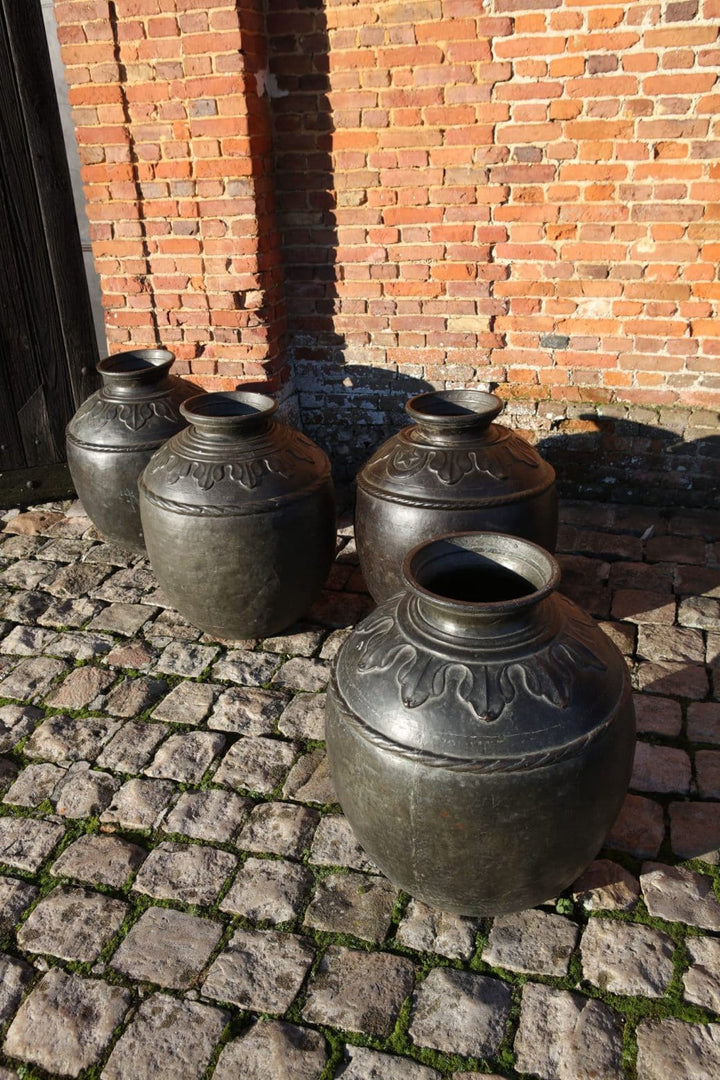 A set of four large vintage Sindh bronze pots on cobblestone with brick wall background by Collection EE10