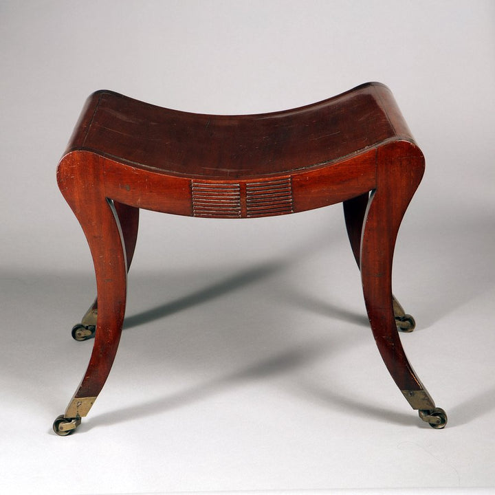 Regency mahogany sabre legged saddle stool with brass casters from Collection TH10 showcasing elegant craftsmanship