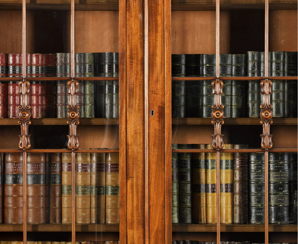 Close-up of Regency mahogany breakfront bookcase by Nwtiques showcasing carved details and antique books behind glass doors