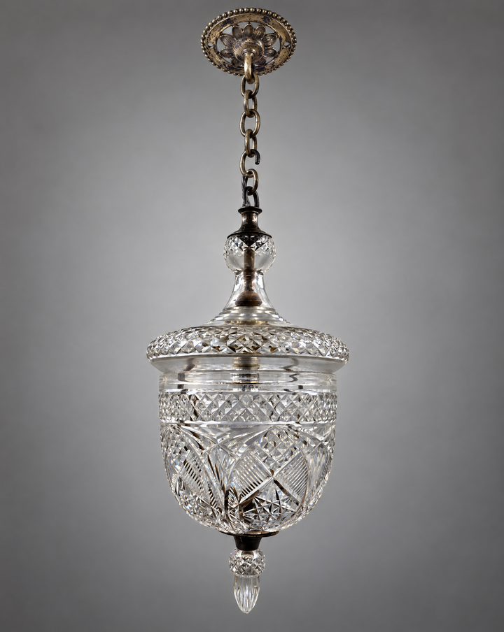 An antique cut glass pendant light with ornate silvered metal hardware, hanging against a neutral gray background.