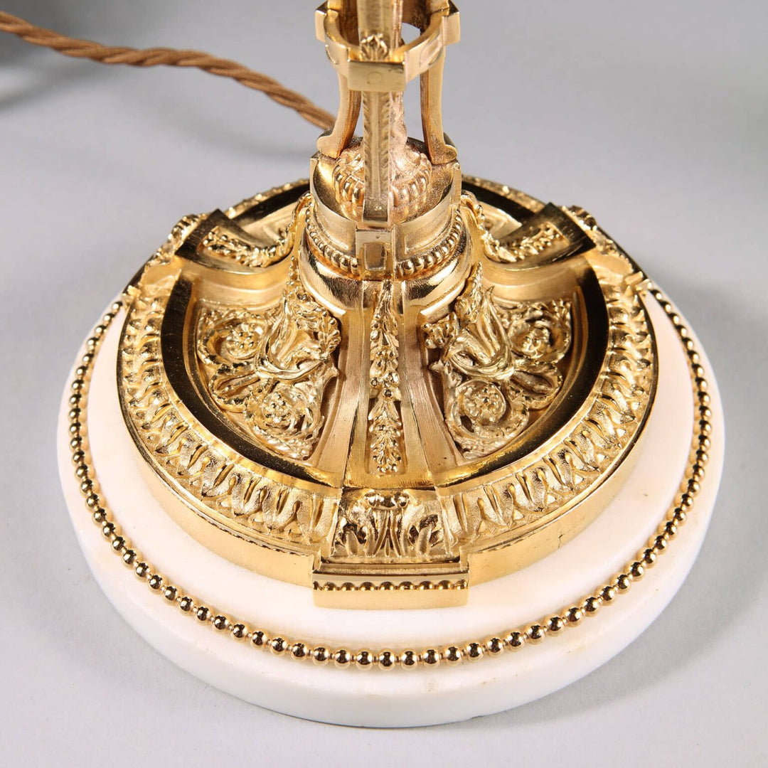 Pair of French Gilt Bronze Neo Classical Candlestick Table Lamps with ornate gold detailing on white marble base.