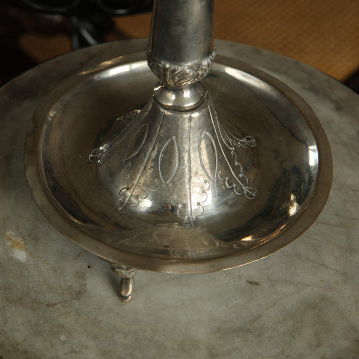 Close-up of a European silver candlestick base with intricate foliate engraving from Collection EE10 on marble surface