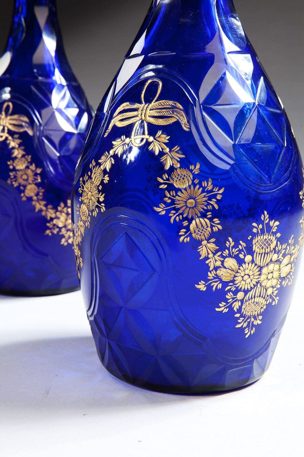 Pair of blue glass facet cut decanters with gold floral detailing from Collection TH10 displayed on white background