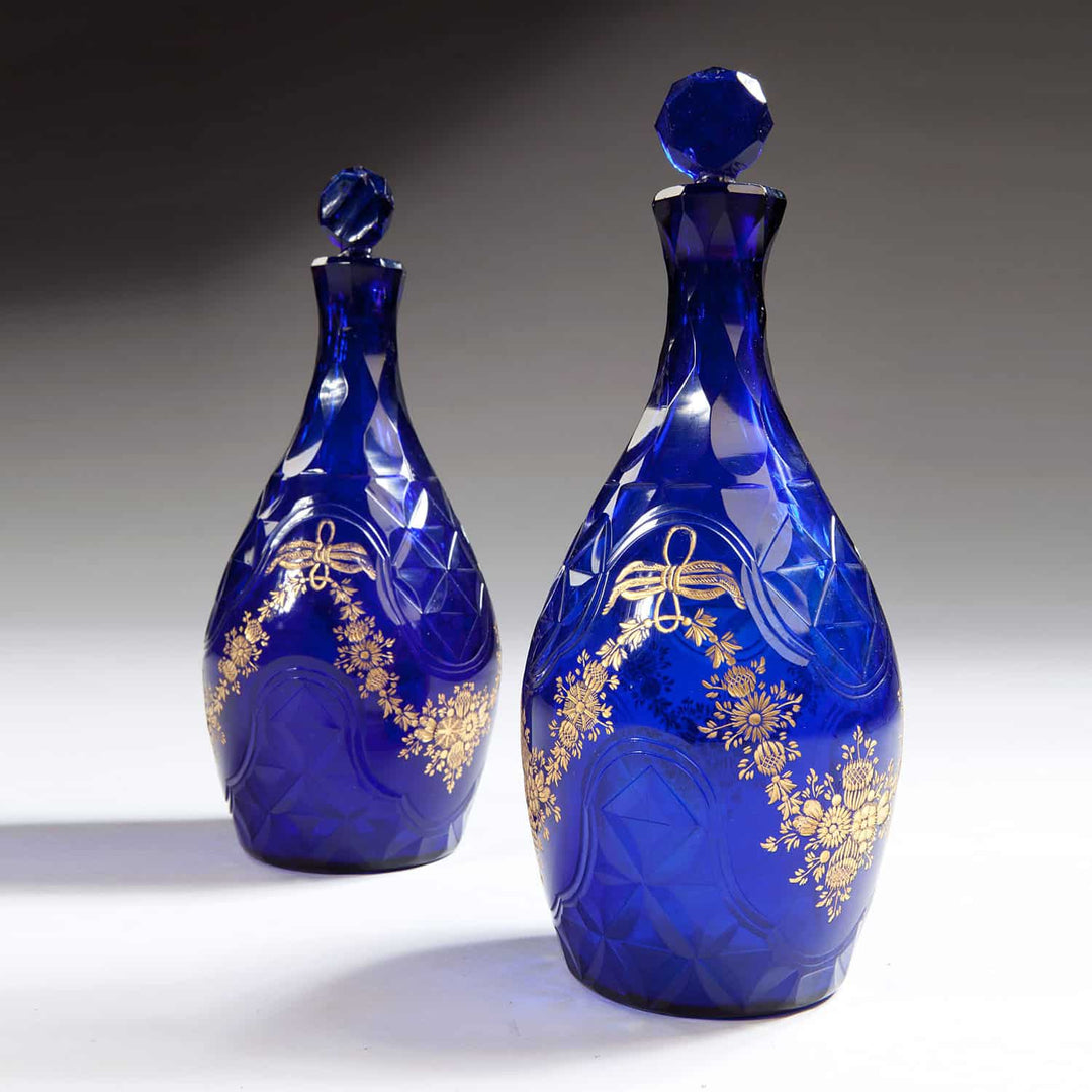 Pair of elegant blue glass facet cut decanters with gold floral detailing from Collection TH10 displayed on neutral background
