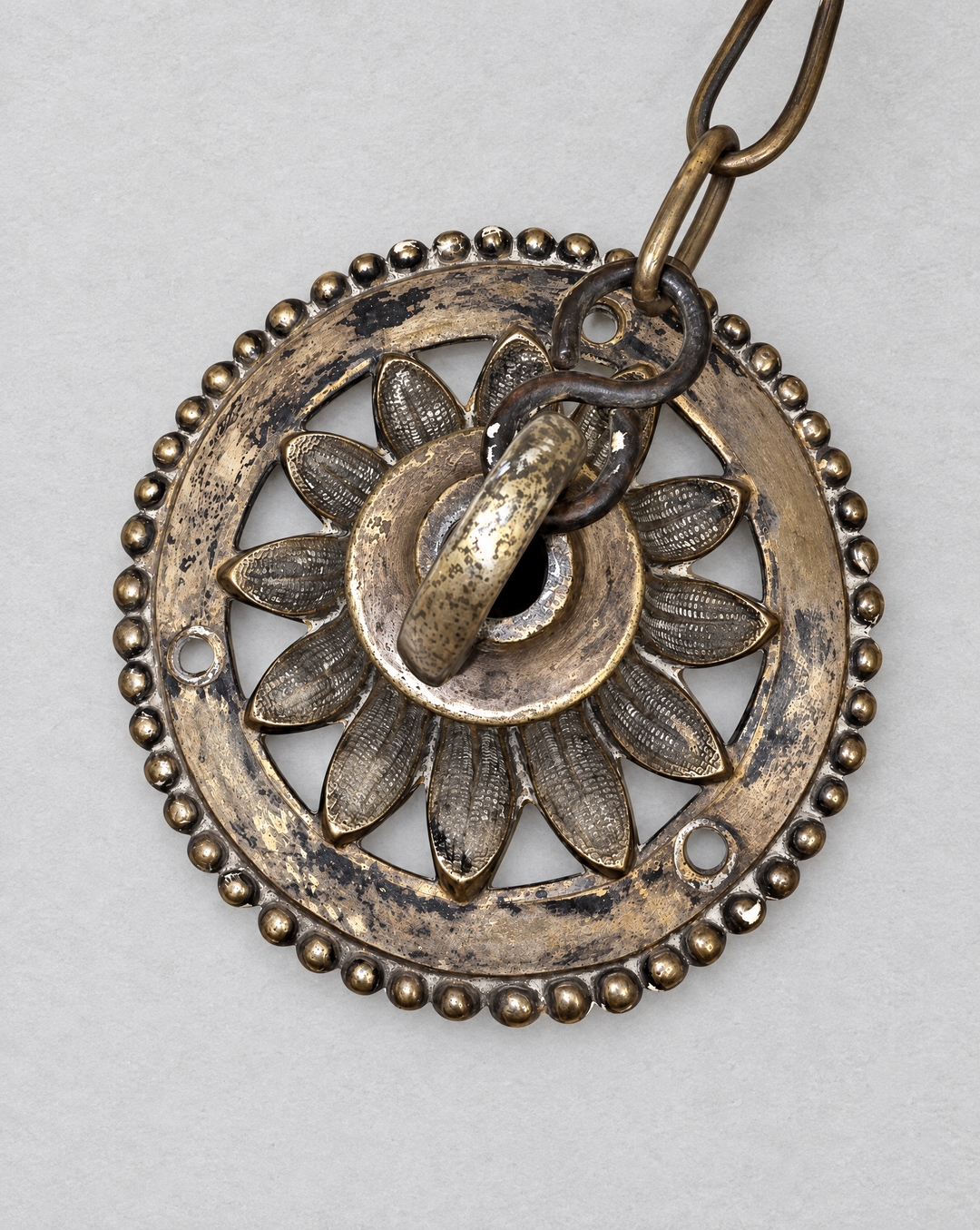 Silvered ceiling hook with a circular beaded border, a flower-like cutout center, and a hanging loop attached at the top, shown on a plain light background. By Osler 
