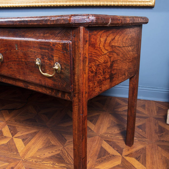 Close-up of highly figured elm wood dresser base with brass drop handle from Collection CK20 against blue wall and parquet floor