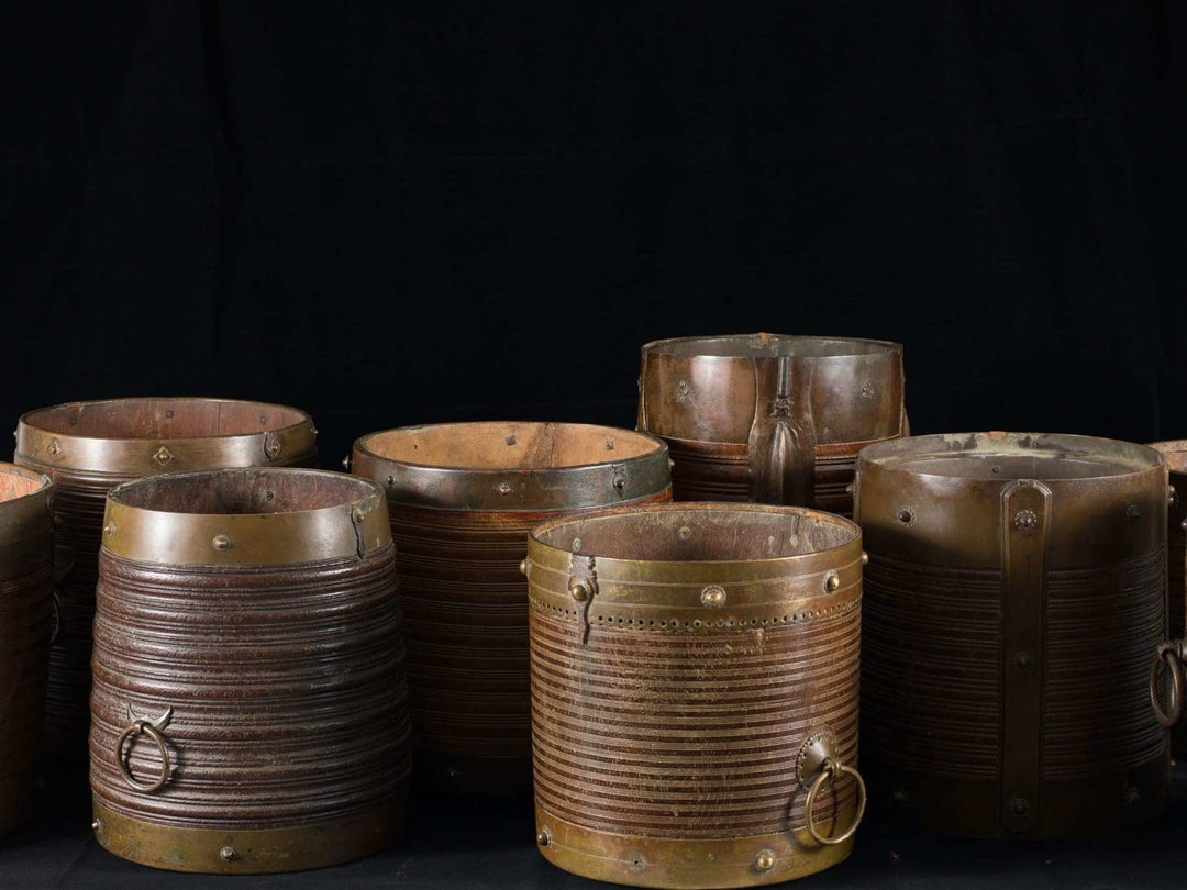 Collection EE20 nine 19th century Indian teak rice measures with brass mounts and handles displayed on black background