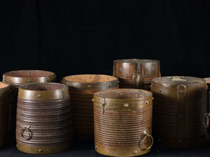 Collection EE20 nine 19th century Indian teak rice measures with brass mounts and handles displayed on black background